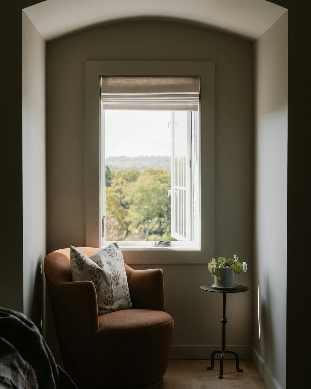 Une femme lit dans un fauteuil, près d'une fenêtre lumineuse, une tasse à la main